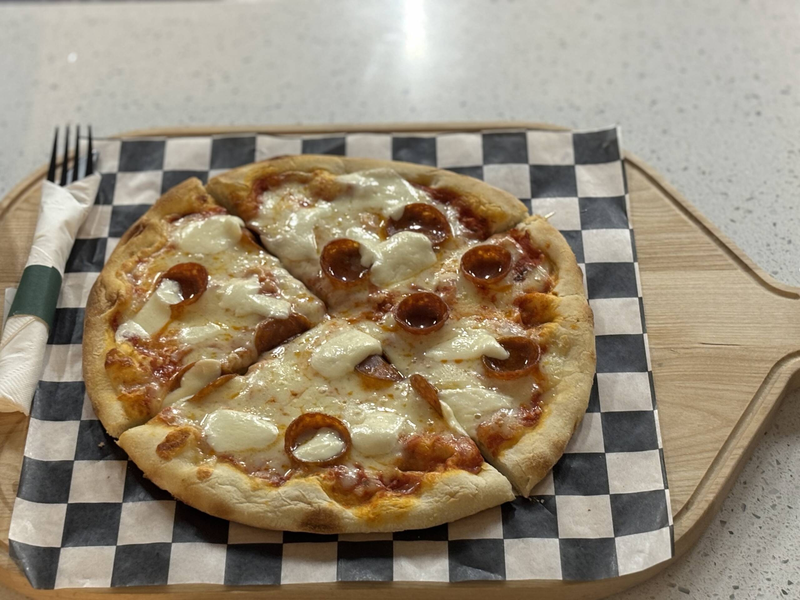 A small, personal-sized pizza topped with melted mozzarella cheese and pepperoni slices, served on a wooden board in the HV Pickleball & Golf Center lounge.
